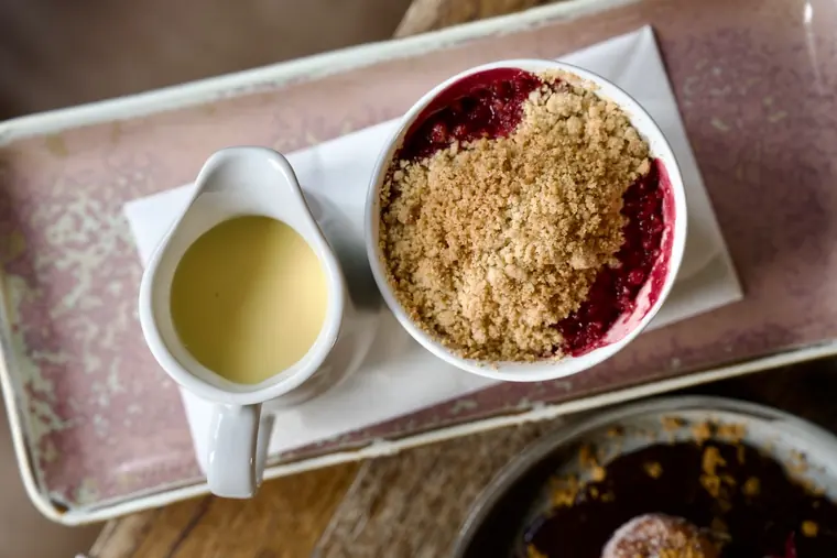 Apple and raspberry crumble served with a jug of custard