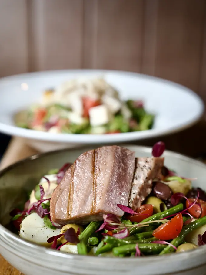 A warm salad topped with sliced pork belly