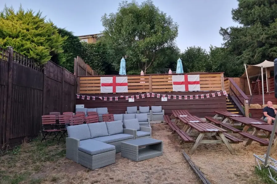 The wider garden: sofas, picnic benches and parasols against a wooden fence