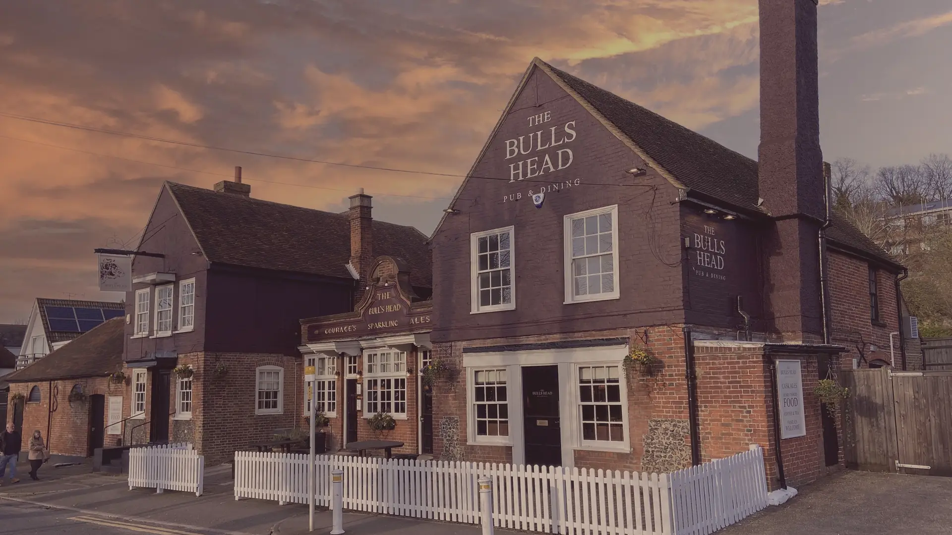 The Bull's Head at dusk, a brick and weatherboard village pub under a pink sky