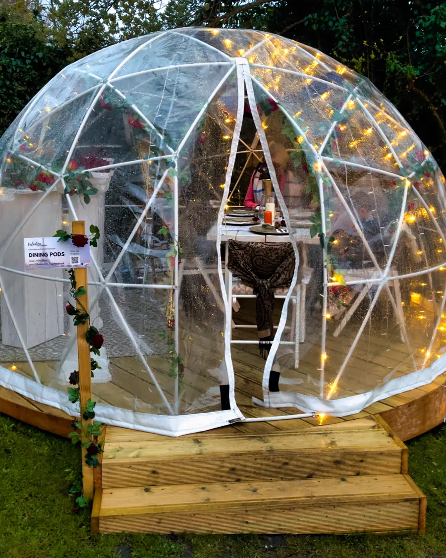 A lit geodesic dining pod in the garden, laid for dinner