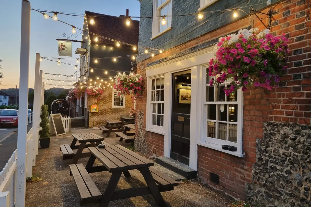 Picnic benches along the side of the pub under strung lights, early evening